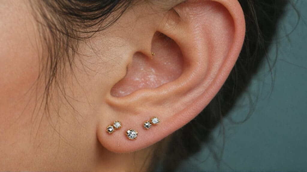 Close-up of ear showing multiple healed piercings with gold and crystal stud earrings in lobe and cartilage