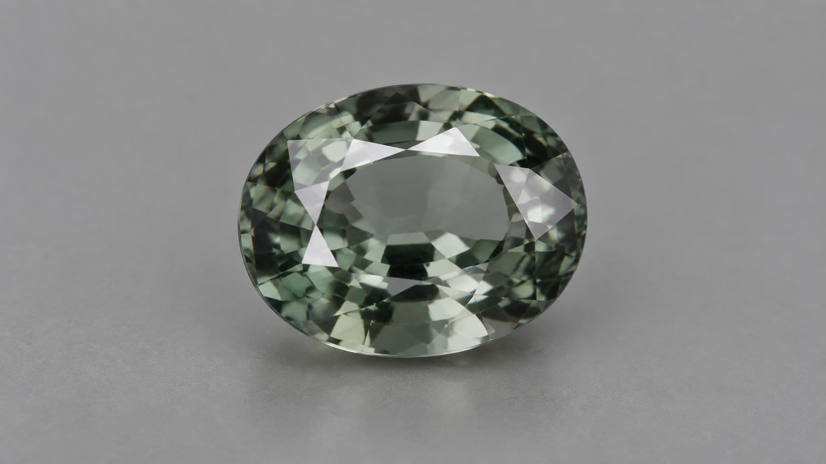 Faceted green-gray musgravite gemstone on a neutral gray background