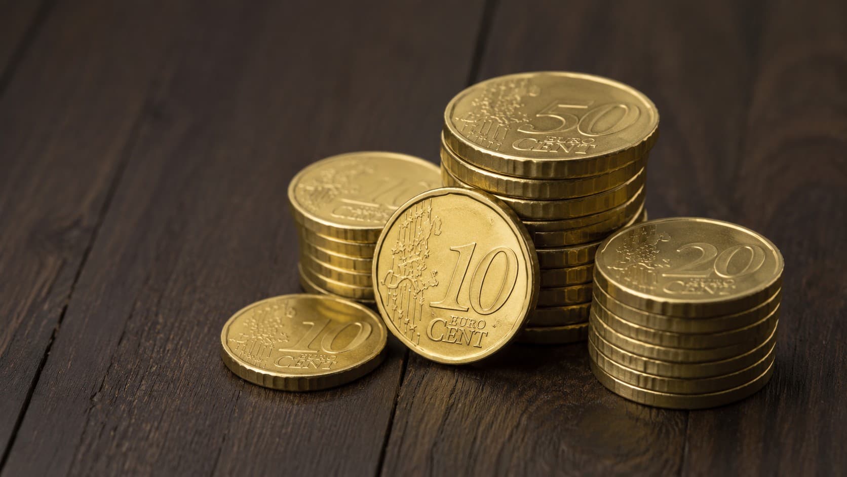 Stacked 10, 20, and 50 euro cent coins made of Nordic gold on a dark wooden surface