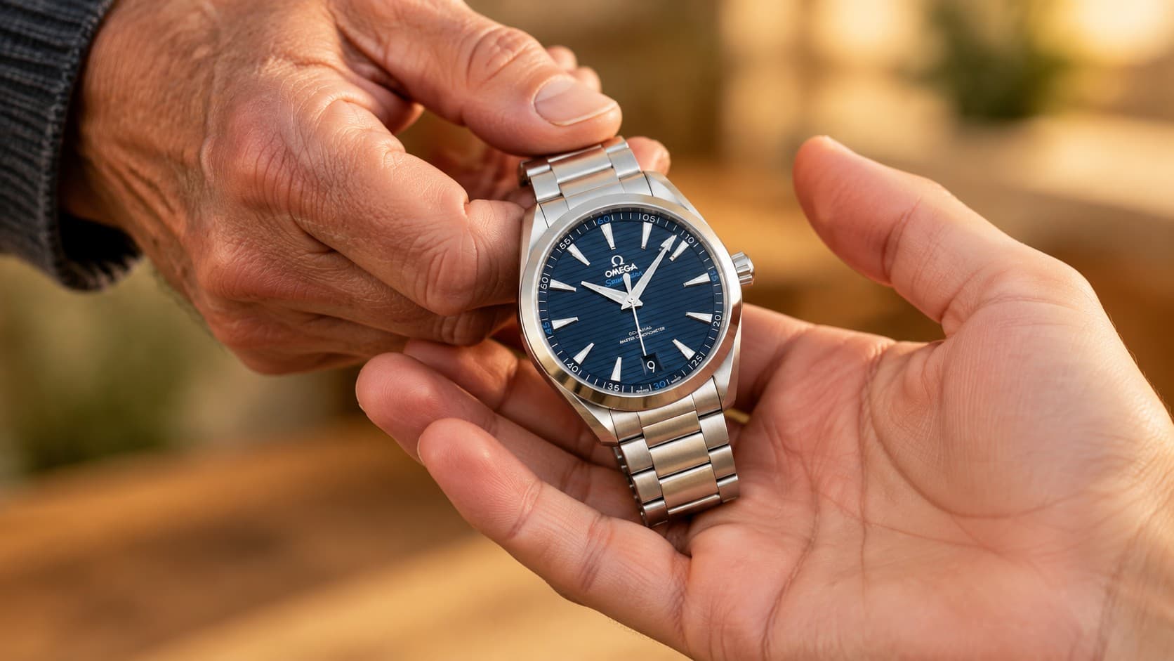 Older hand passing an Omega Seamaster Aqua Terra watch to a younger hand