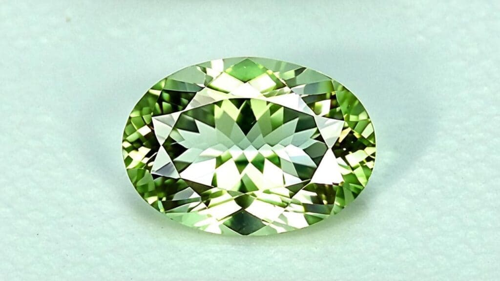 An oval-cut green sillimanite gemstone with high clarity and intricate faceting, reflecting light on a white background.
