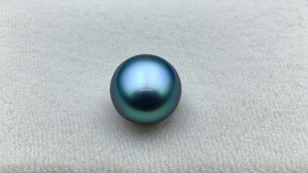 Close-up of a peacock-colored Tahitian black pearl with green, blue, and purple overtones on a light background.