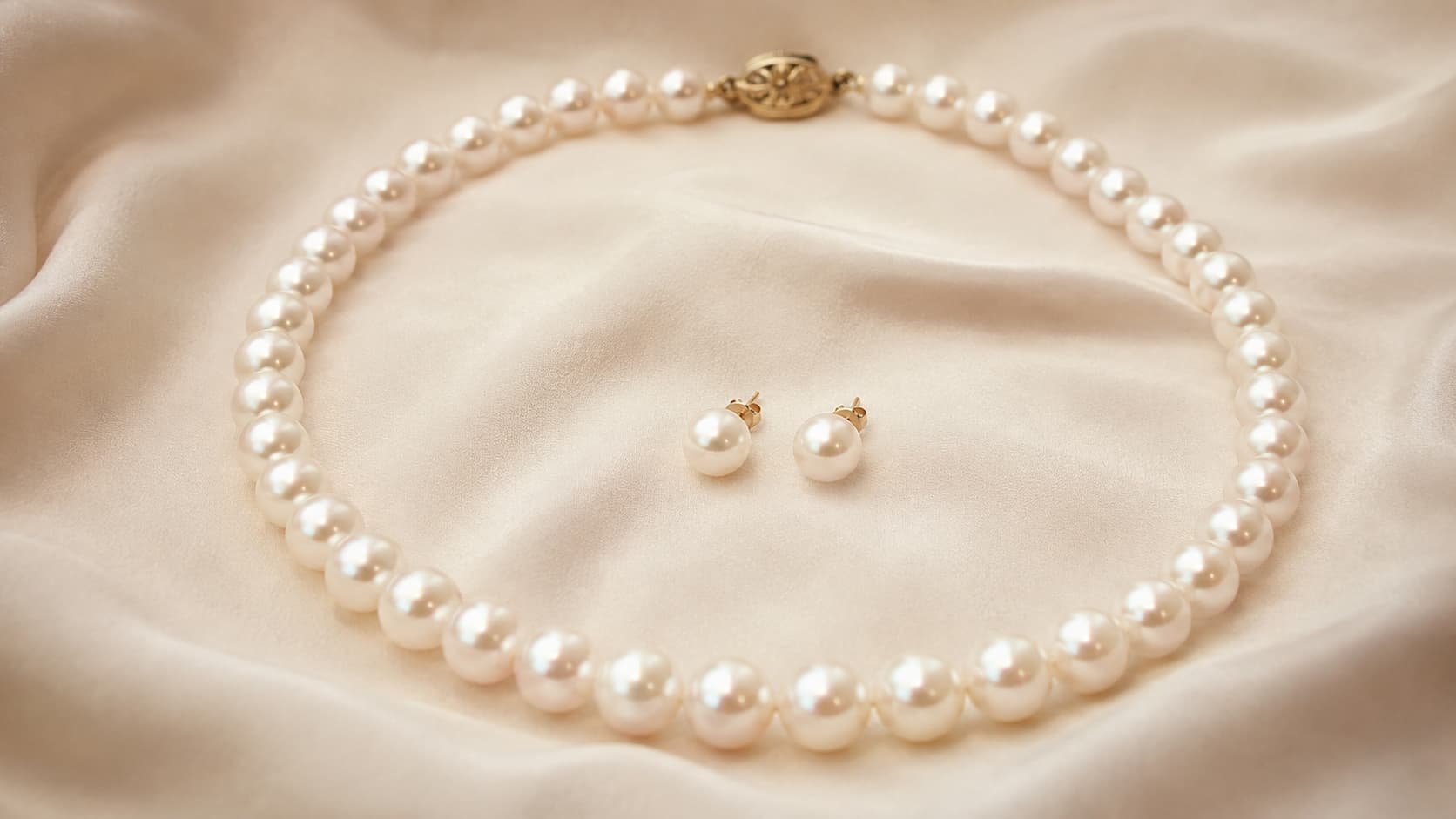 Classic 1950s pearl necklace with matching pearl stud earrings on cream fabric