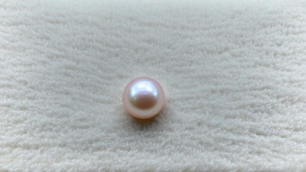 Close-up of a pink freshwater pearl with soft blush tones and natural luster resting on a white textured surface.