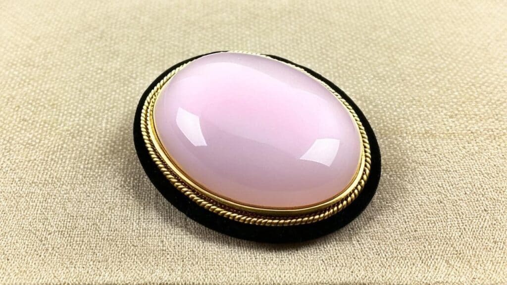 Smooth polished rose quartz cabochon set in an ornate vintage gold bezel, displayed on neutral fabric.