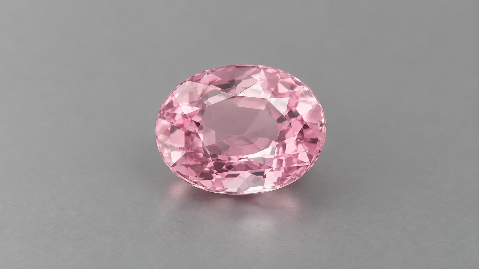 Faceted pink poudretteite gemstone on a neutral gray background