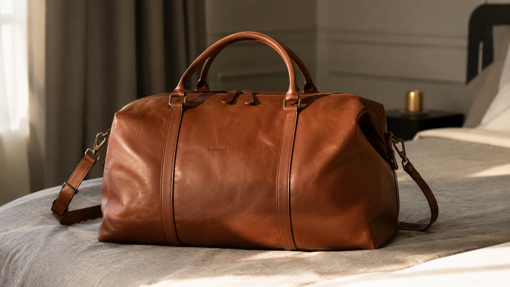 Brown genuine leather duffel bag with stitched handles resting on a bed