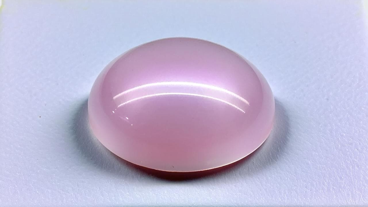 Oval rose quartz cabochon with a smooth polished dome on white