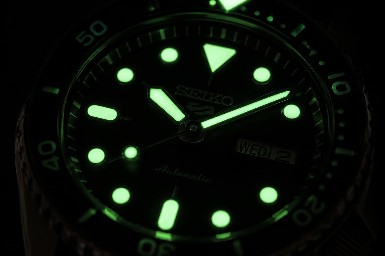 Seiko dive watch dial glowing bright green in the dark, showing Super-LumiNova lume on the hands and markers