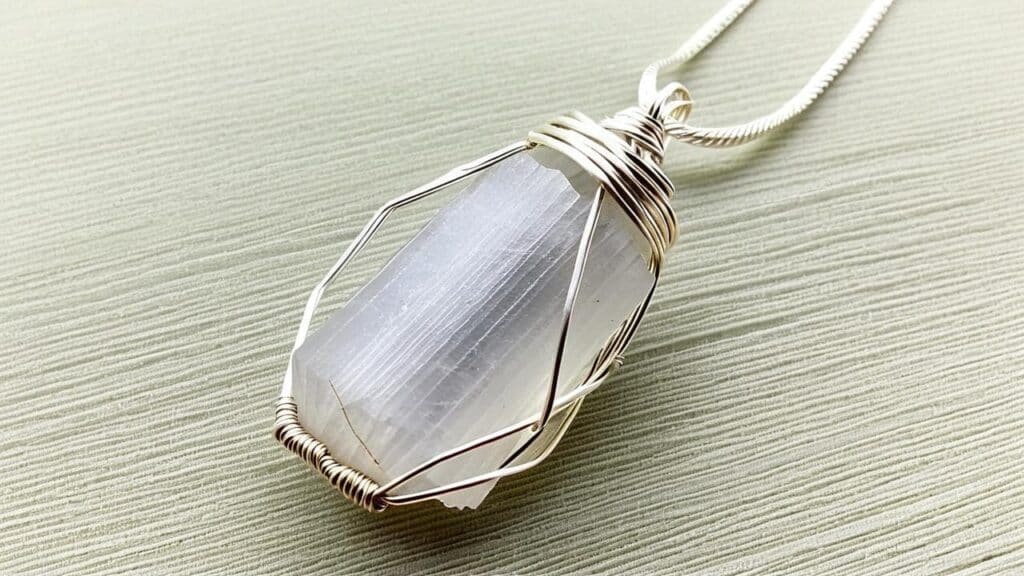 Selenite crystal pendant in silver wire cage setting on textured background
