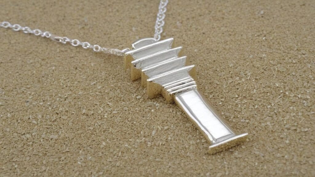 Silver Djed pillar pendant on a delicate chain, displayed on a sandy background, representing the ancient Egyptian symbol of stability and rebirth.
