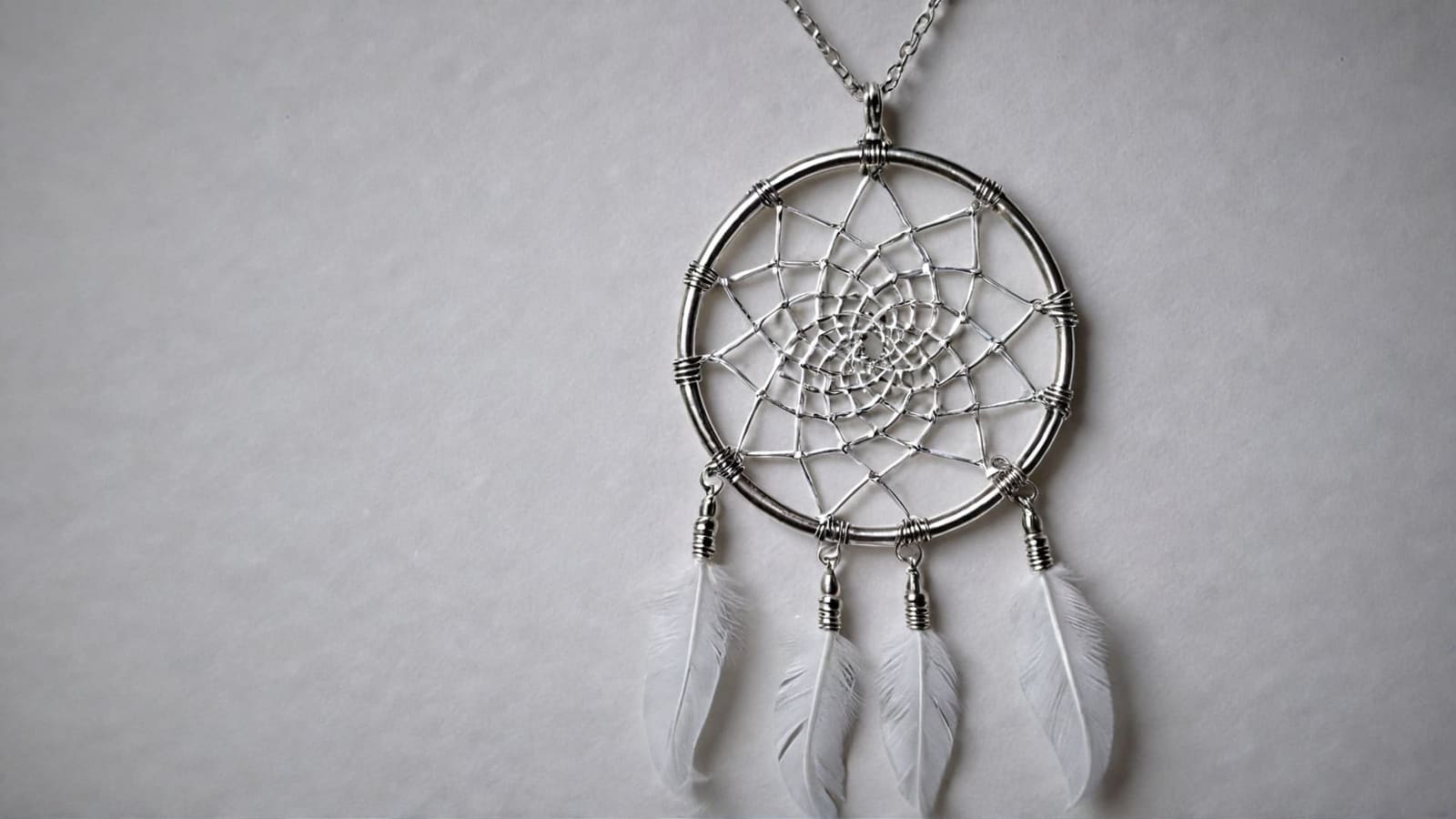 Silver dreamcatcher pendant with woven web and small white feathers