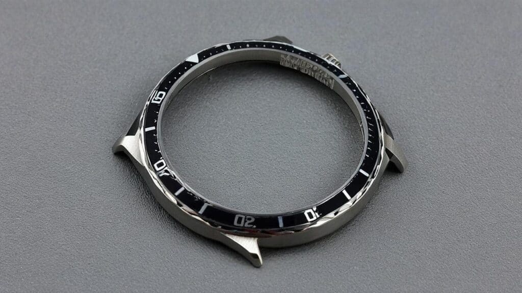 Scratched silver dive watch bezel with black timing markings showing wear and damage on metal surface