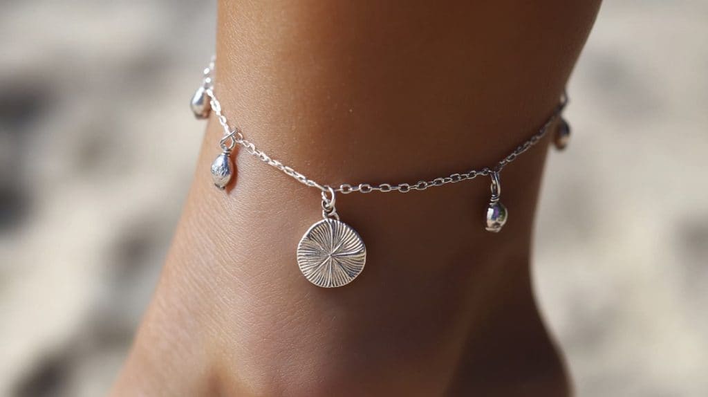 A delicate silver anklet featuring a sand dollar charm and small dangling accents, perfect for beach-inspired fashion.