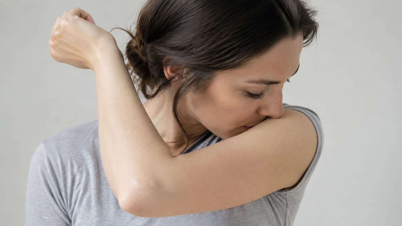 Woman with her eyes closed smelling the bare skin of her inner elbow to reset her sense of smell