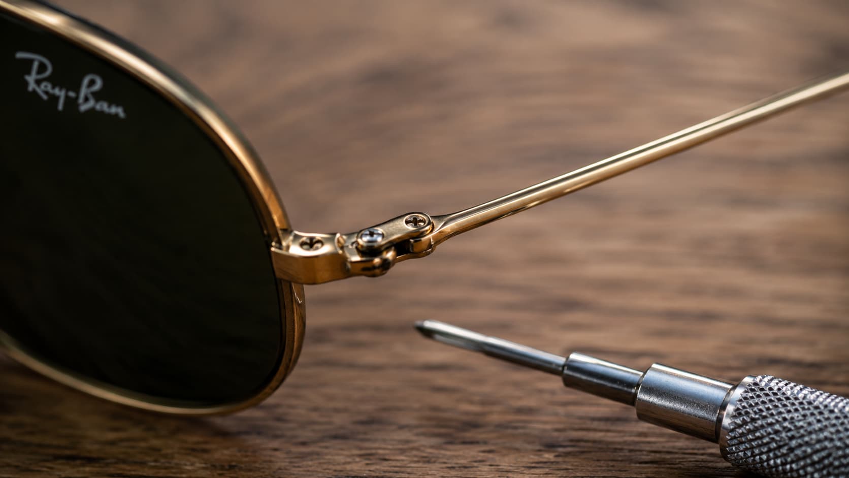 Close-up of a sunglasses hinge being tightened with a small screwdriver