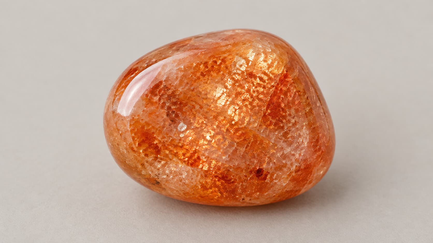 Close-up of a tumbled sunstone gemstone showing glittery aventurescence inclusions