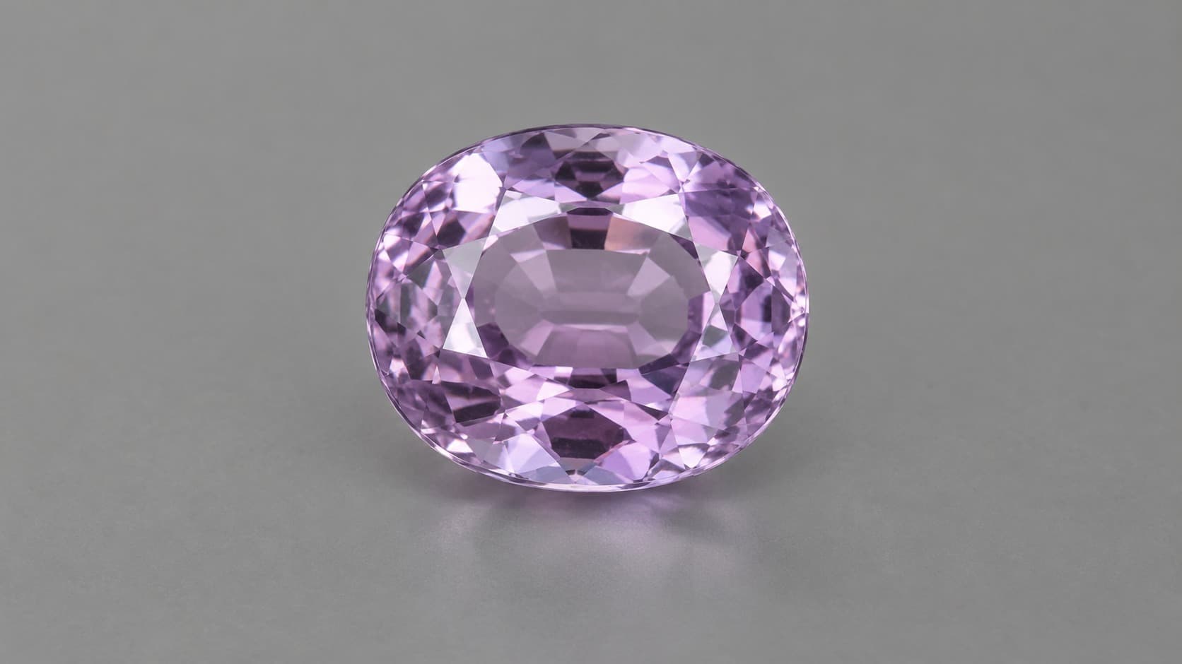 Faceted violet-purple taaffeite gemstone on a neutral gray background