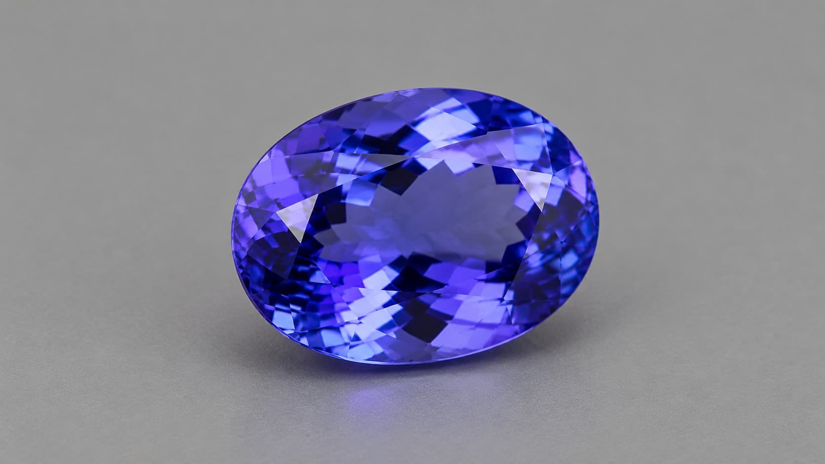 Faceted violet-blue tanzanite gemstone on a neutral gray background