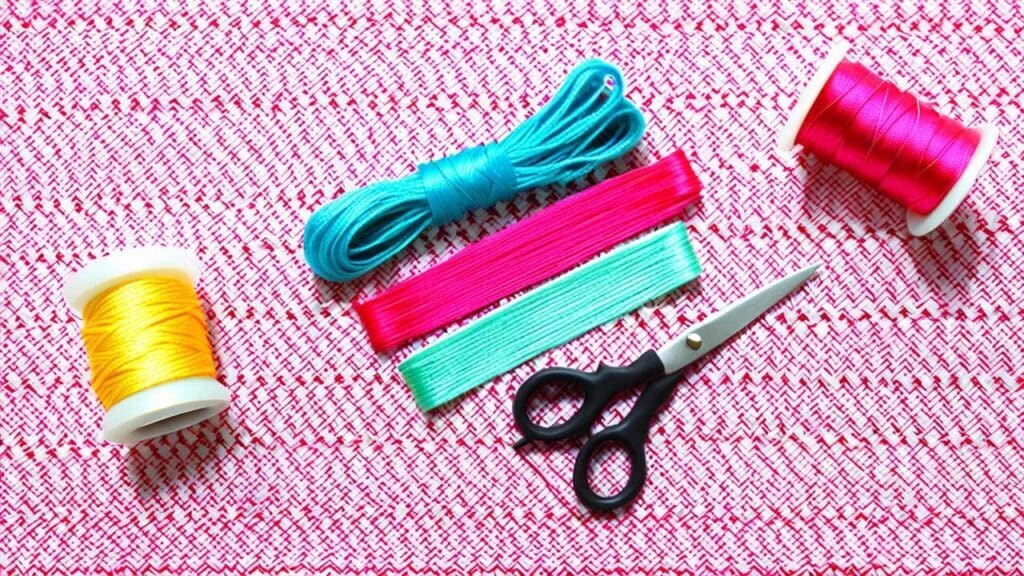 Colorful embroidery floss, scissors, and thread spools laid out for making handmade thread bracelets.
