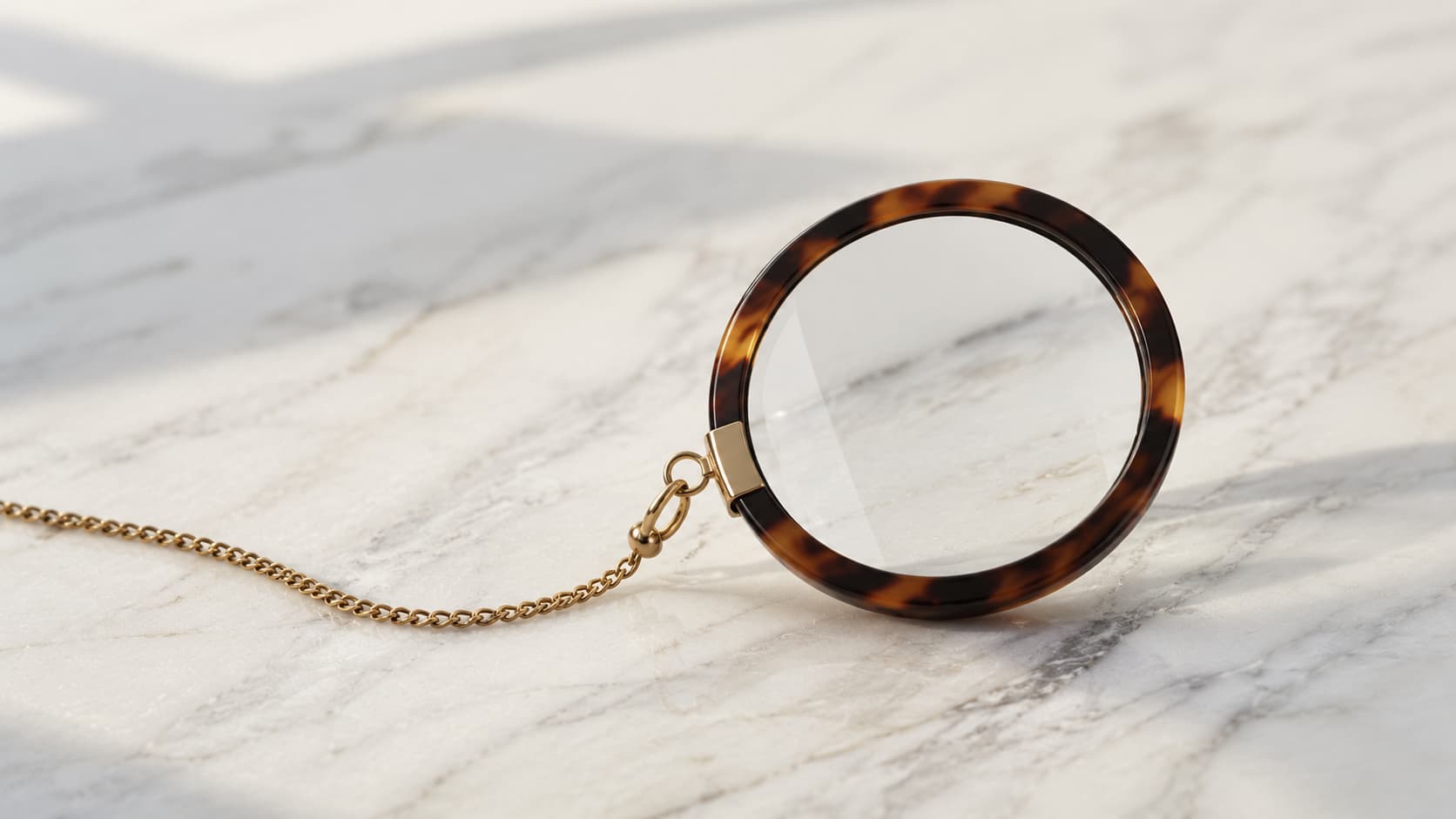 Tortoiseshell monocle with a gold chain resting on a marble surface