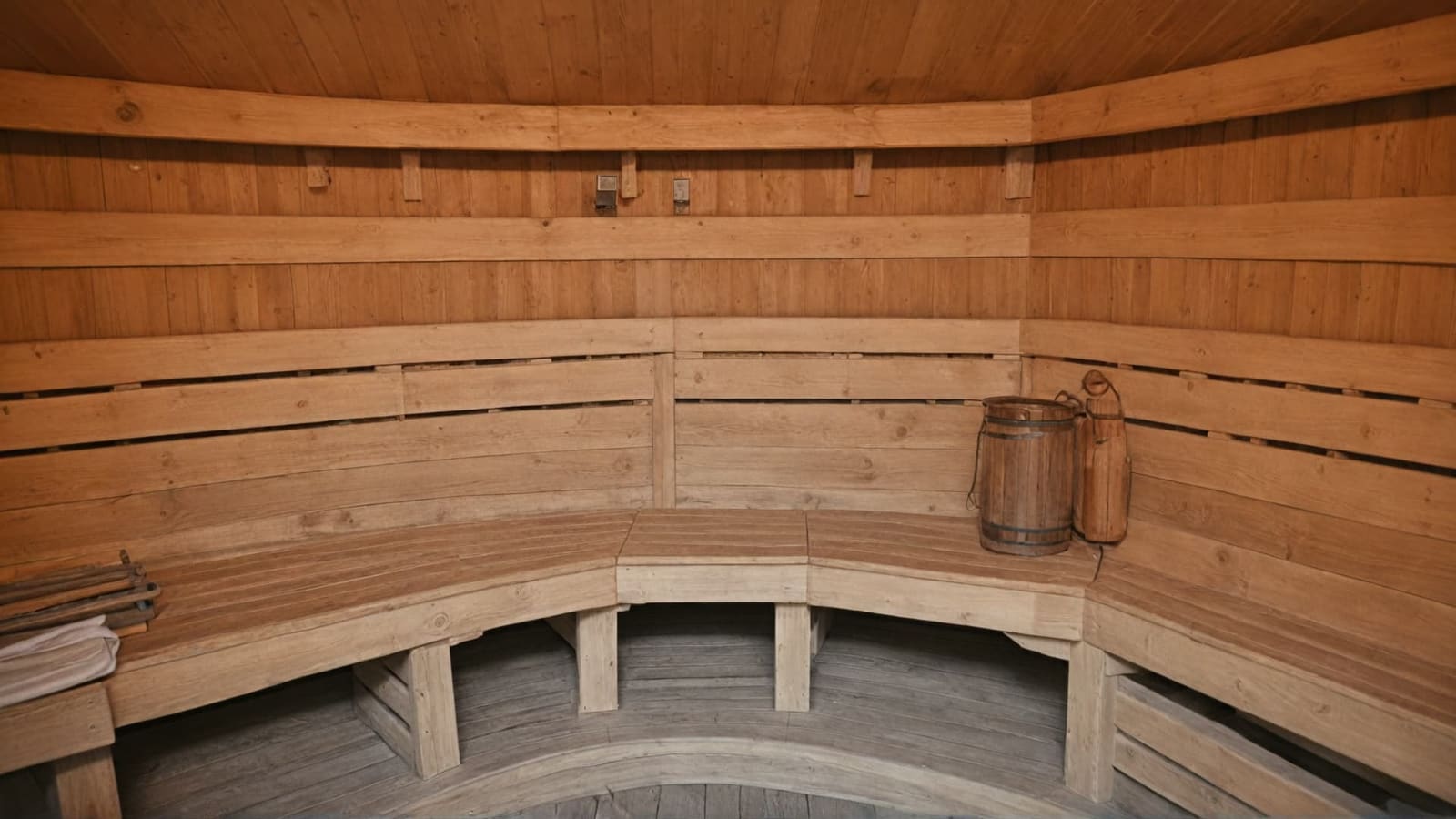 Traditional wooden sauna interior with curved benches and a wooden bucket