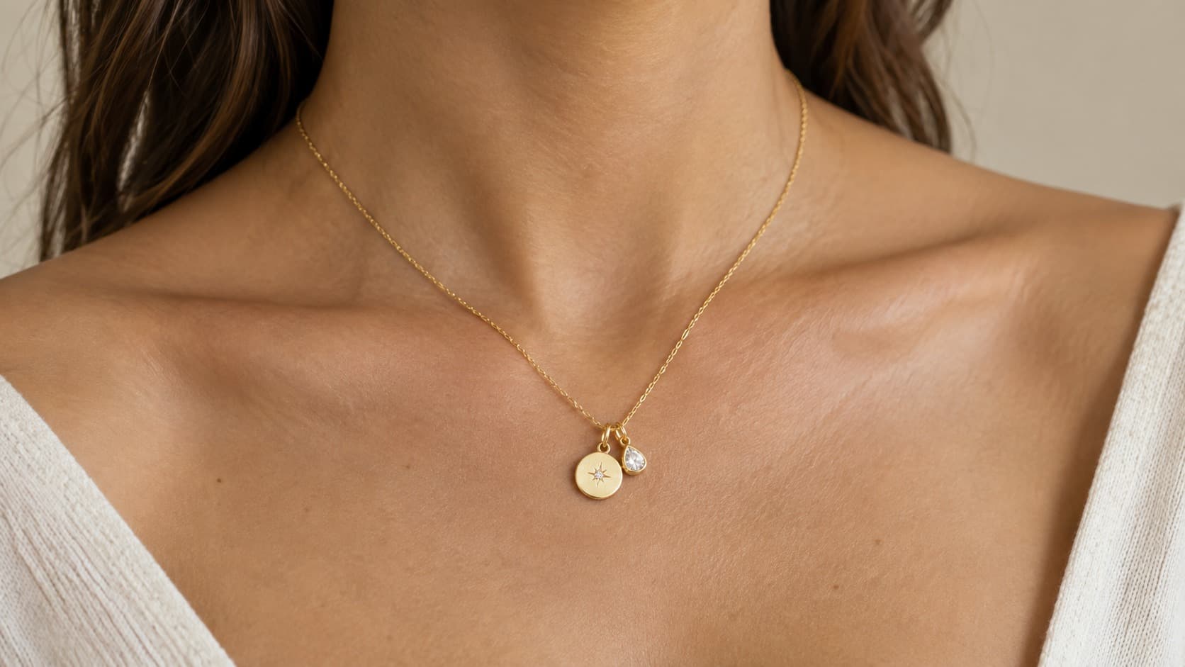 Woman wearing a gold necklace with two pendants, a round star charm and a teardrop crystal, stacked together on one chain