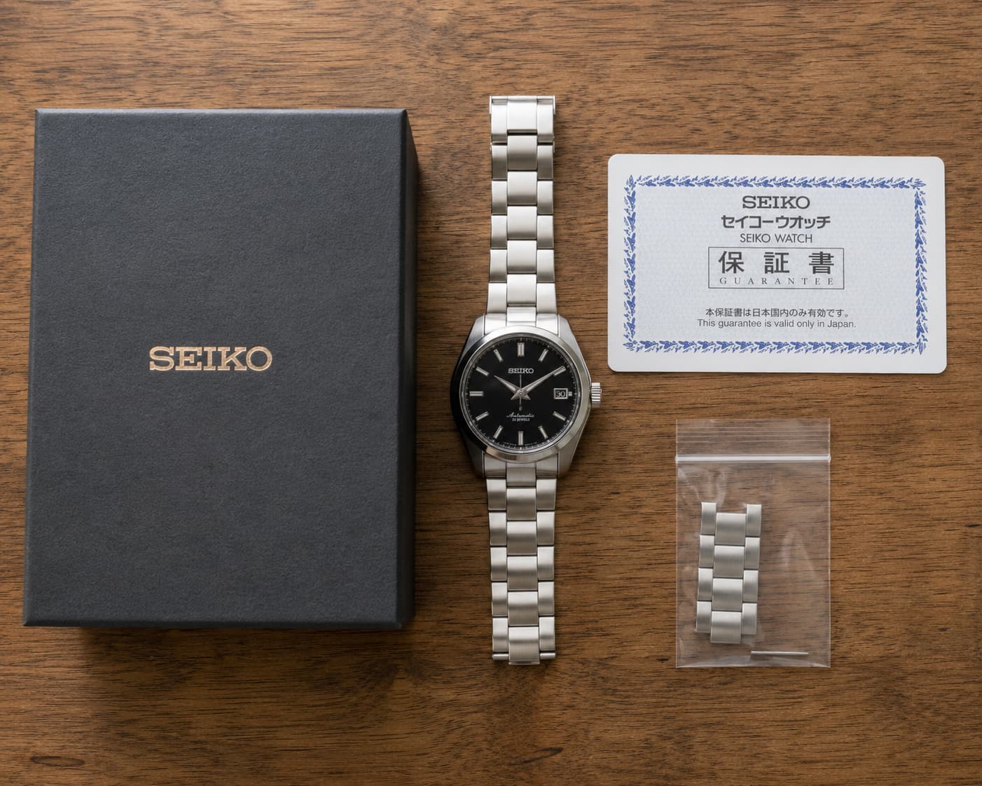 Watch with original box, warranty card, and spare bracelet links laid out on a wooden surface