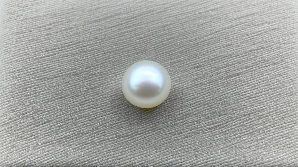 Close-up of a classic white Akoya pearl with a reflective surface and subtle silver overtones on a neutral background.