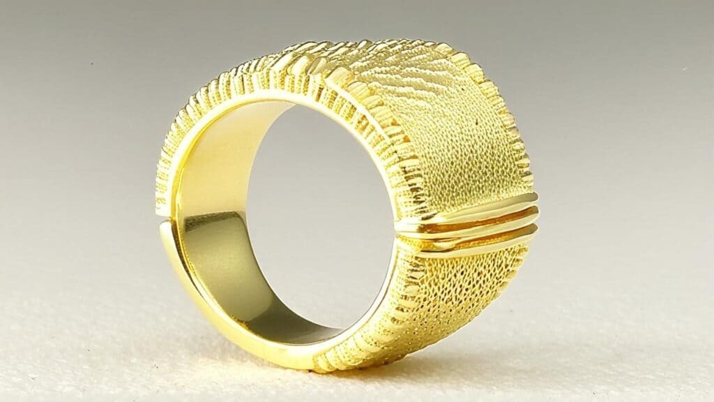 A wide gold band ring created through sandcasting, showcasing intricate textures and a contemporary handcrafted design.
