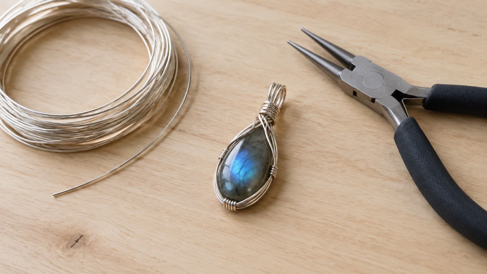 Wire-wrapped labradorite pendant next to silver wire and round-nose pliers