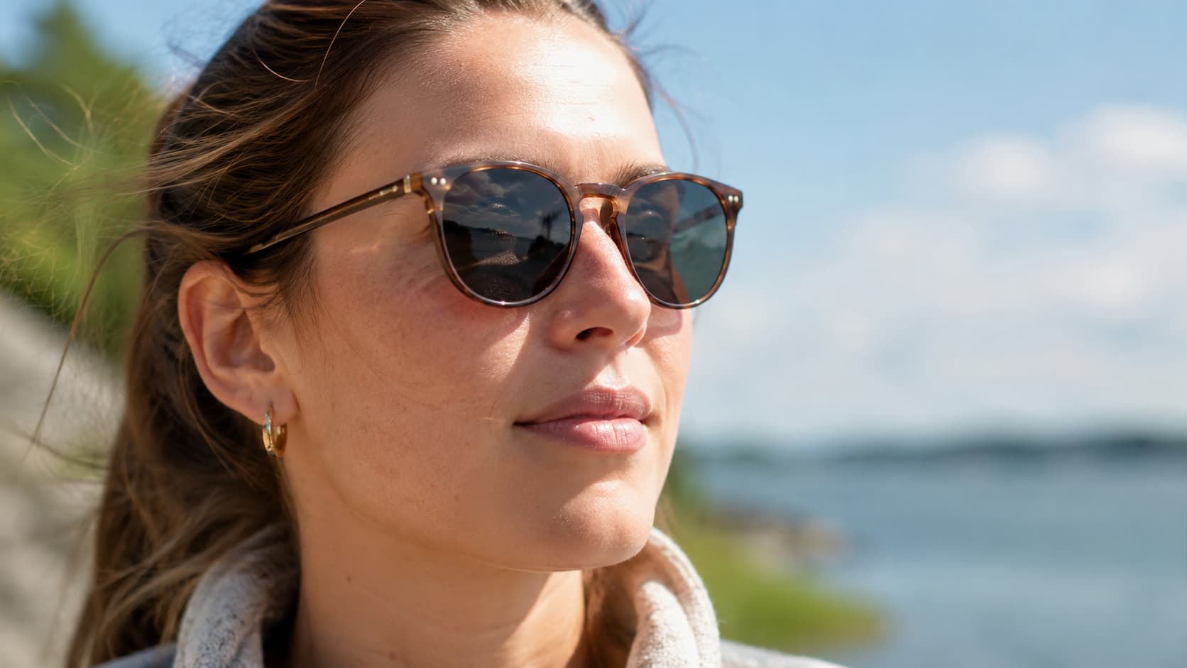 Woman wearing polarized sunglasses outdoors near water on a sunny day
