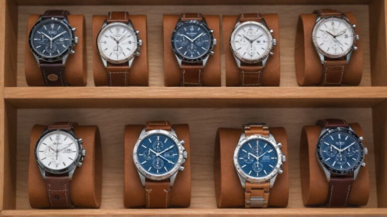 A collection of British luxury chronograph watches with brown leather straps displayed in a wooden watch case.