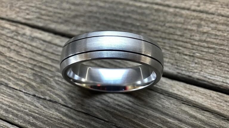 Modern brushed aluminum men's ring with dual grooves, resting on a rustic wooden surface.
