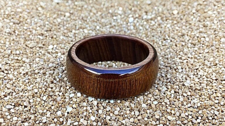A handcrafted wooden ring with a glossy finish resting on a bed of sand, showcasing the rich wood grain and smooth craftsmanship.