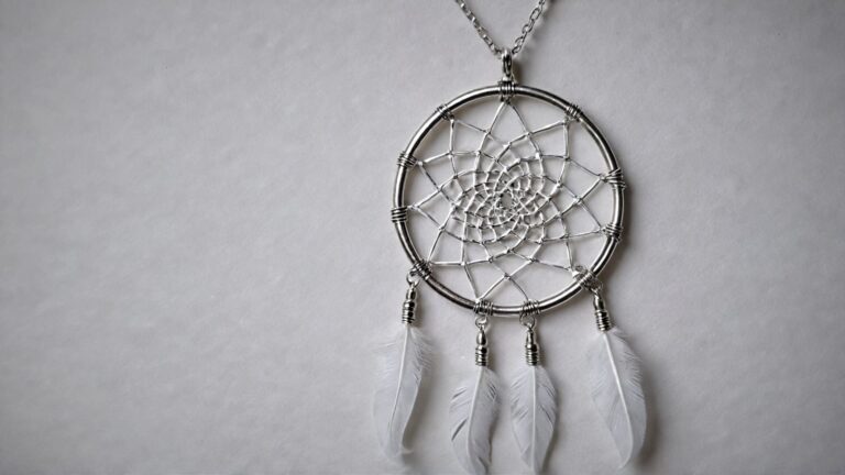 Silver dreamcatcher pendant with white feather charms hanging from a delicate chain, displayed on a neutral background for a minimalist aesthetic.