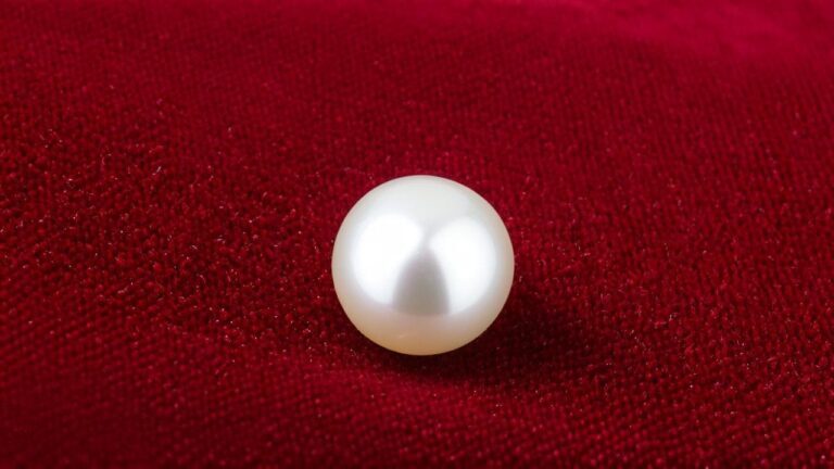 Single cultured pearl with high luster displayed on rich red velvet fabric background.