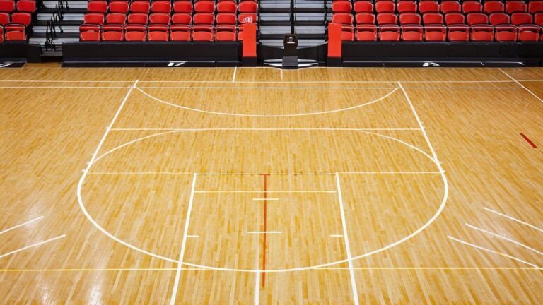 Empty professional basketball court with polished hardwood floor and red stadium seating, where NBA championship teams celebrate their victories.
