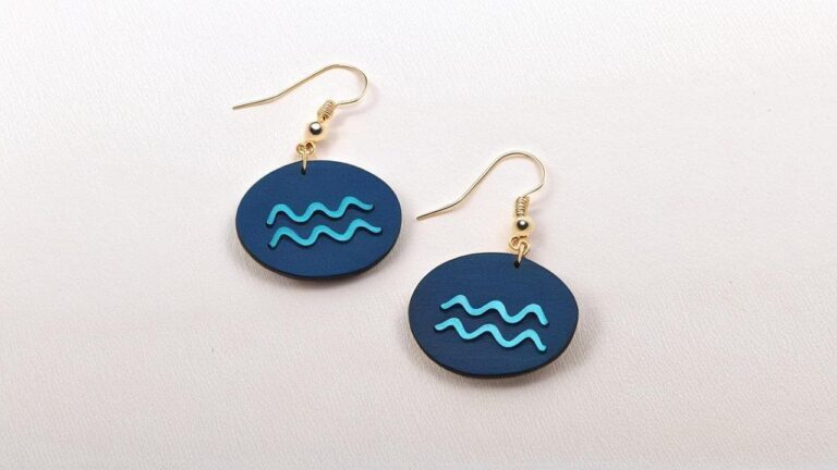 Blue oval Aquarius earrings featuring turquoise wavy symbol design with gold colored hooks on white background