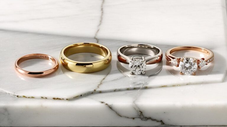 Collection of four different gold rings showcasing yellow gold, white gold, and rose gold options including plain bands and diamond engagement rings on marble surface