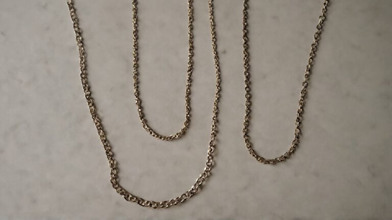 Three gold chain necklaces of varying lengths displayed on marble surface, perfect for layering and length comparison