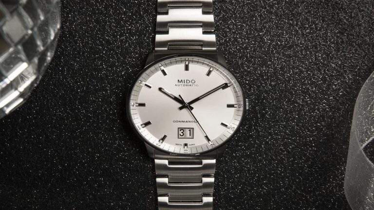 Mido Commander Big Date Swiss automatic watch with silver dial, large date display, and stainless steel bracelet on dark textured background