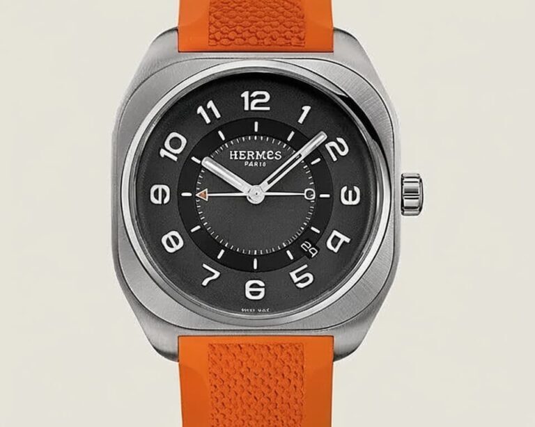 Hermès watch with orange textured leather strap and brushed steel cushion-shaped case on grey background